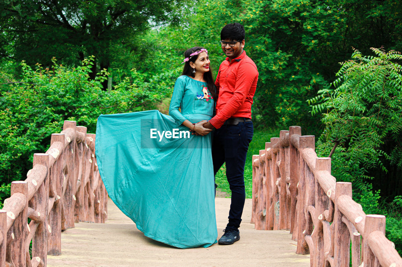 FULL LENGTH OF COUPLE STANDING AGAINST TREES
