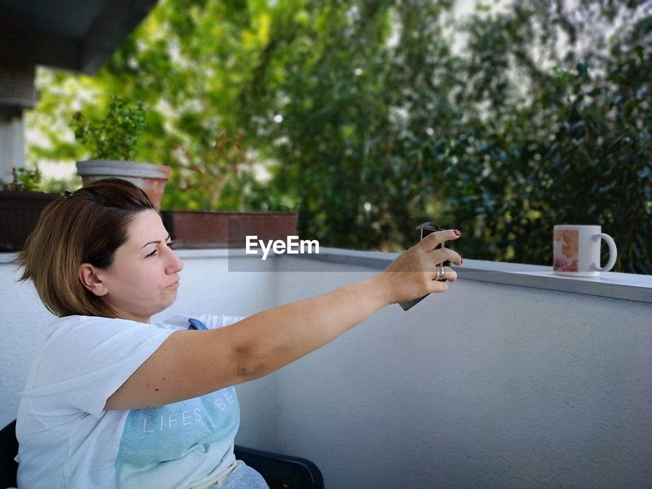 Side view of mature woman taking selfie with smart phone while sitting in balcony