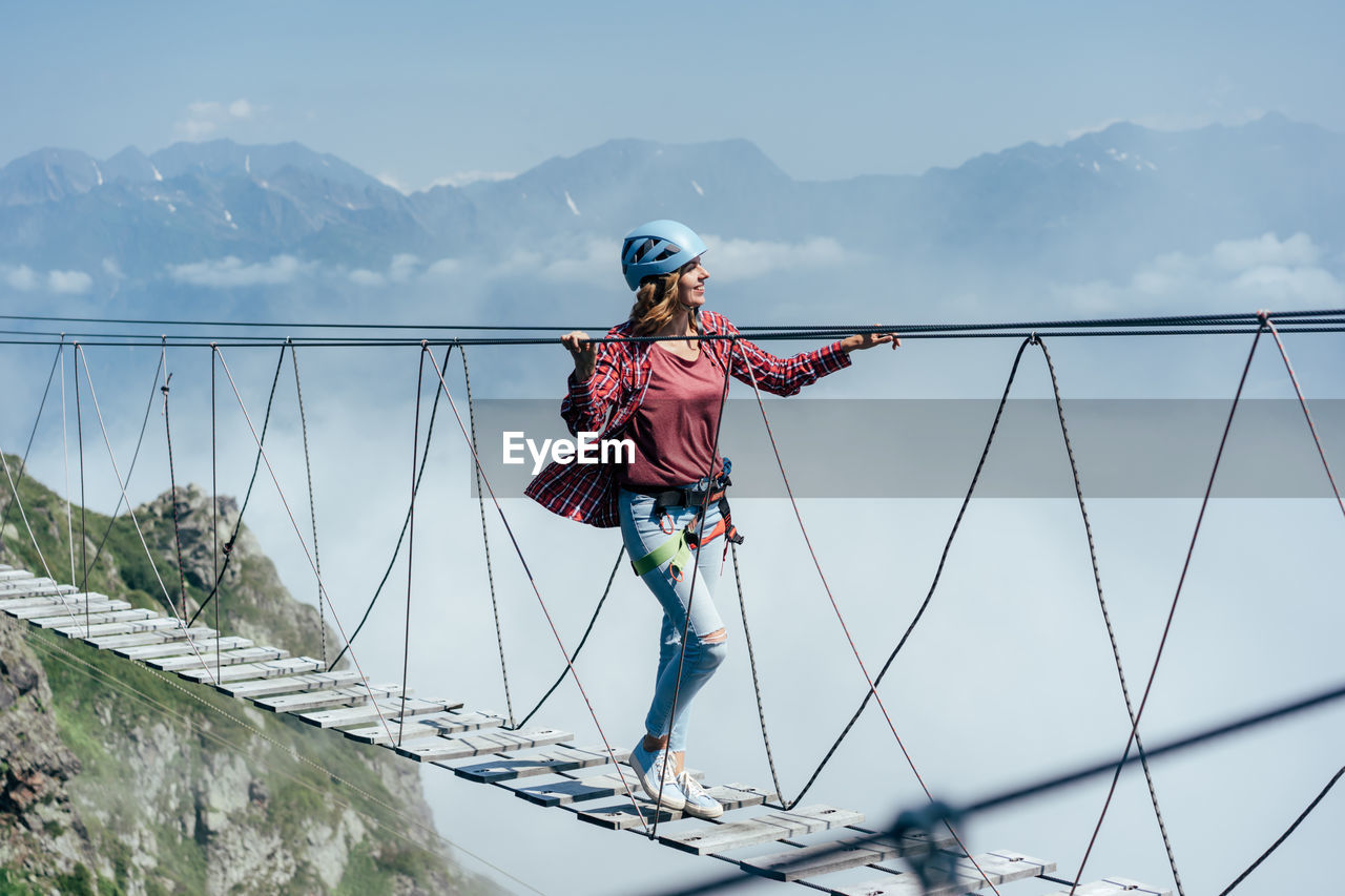 A happy cheerful woman walks on a suspension bridge high in the mountains 