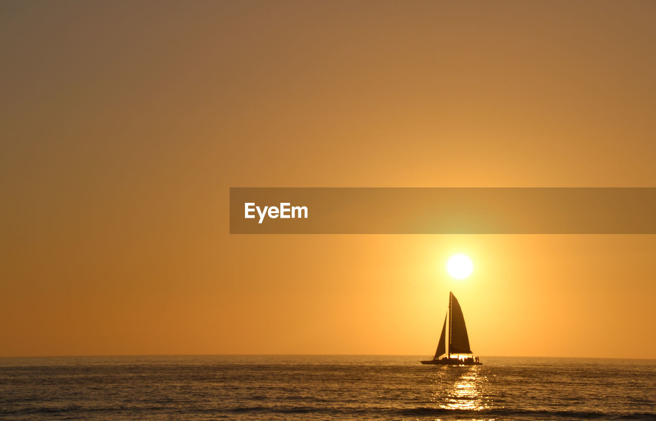 Sailboat sailing on sea against clear sky during sunset
