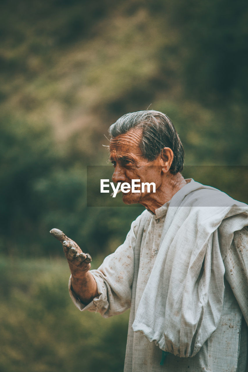 Senior man smoking cigarette while gesturing with dirty hands