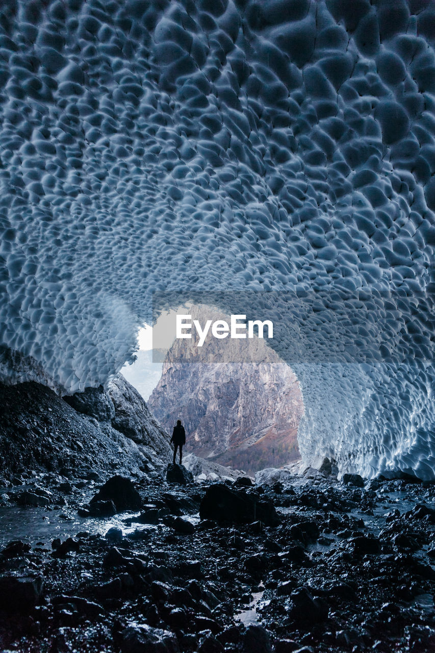 Rear view of silhouette person standing in frozen cave