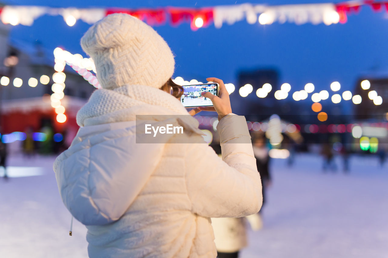 MAN PHOTOGRAPHING ILLUMINATED CITY IN WINTER