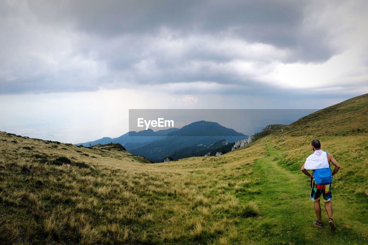 Rear view of man walking on mountain against cloudy sky