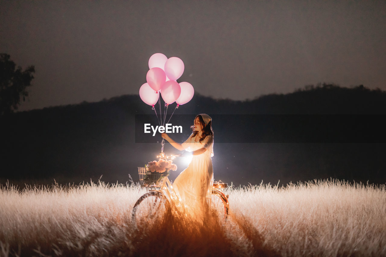 SIDE VIEW OF A PERSON HOLDING BALLOONS AT FIELD