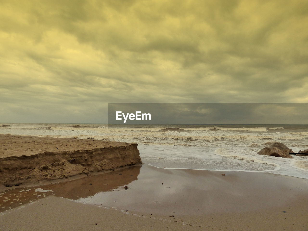 Scenic view of shore at beach against cloudy sky