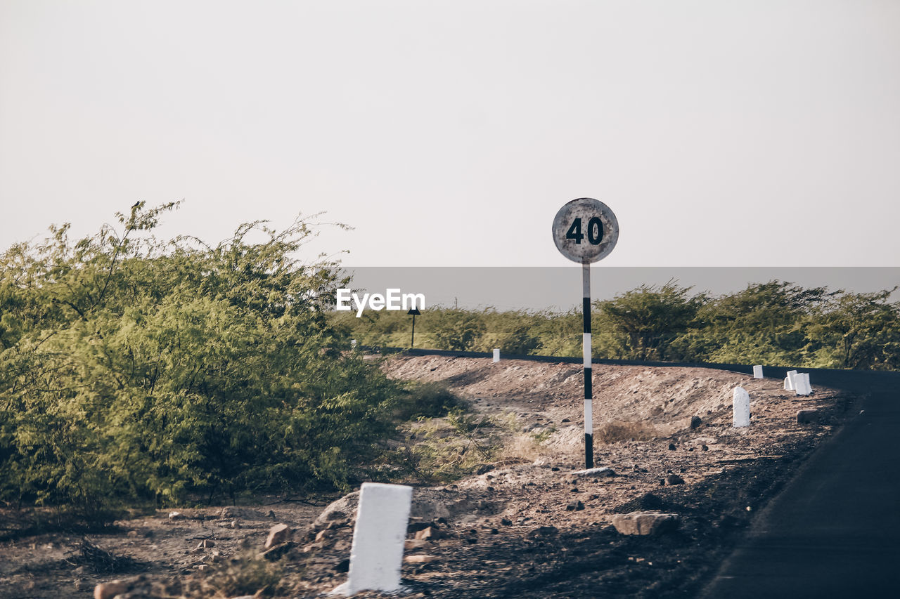 ROAD SIGN BY TREES AGAINST SKY