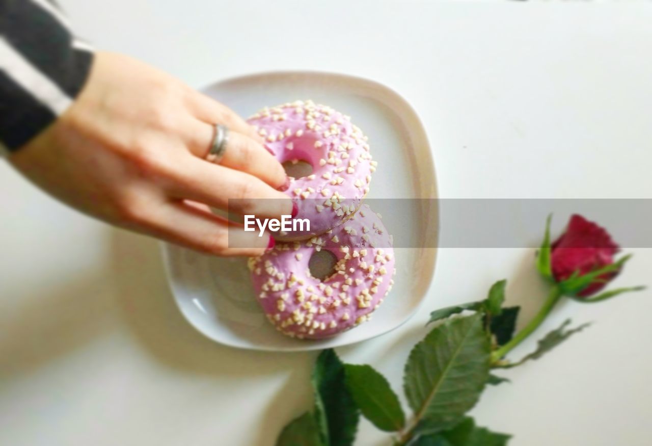 Cropped hand of woman holding donut in plate by rose on white table