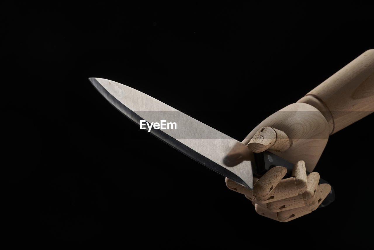 Sharp knife in wooden hand in studio on black background demonstrating concept of violence