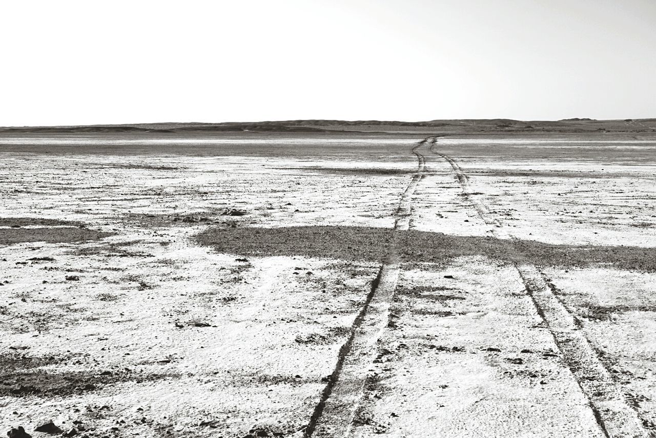 Tire tracks on desert against sky during winter