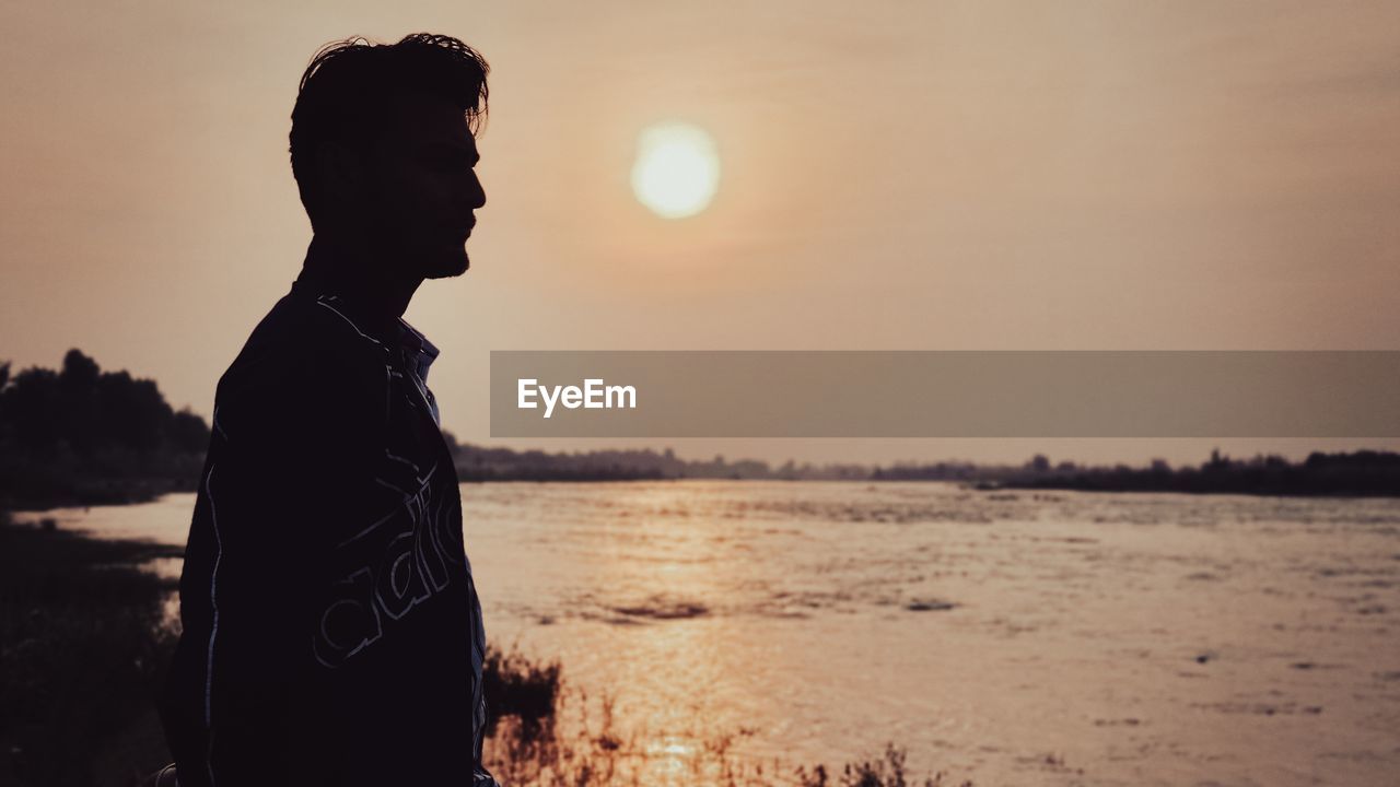 sky, water, one person, sunset, beach, nature, land, sea, adult, silhouette, tranquility, side view, standing, backlighting, beauty in nature, contemplation, sunlight, young adult, leisure activity, lifestyles, men, tranquil scene, outdoors, solitude, vacation, back lit, evening, person, three quarter length, relaxation, sun, trip, waist up, holiday, scenics - nature, copy space, dusk