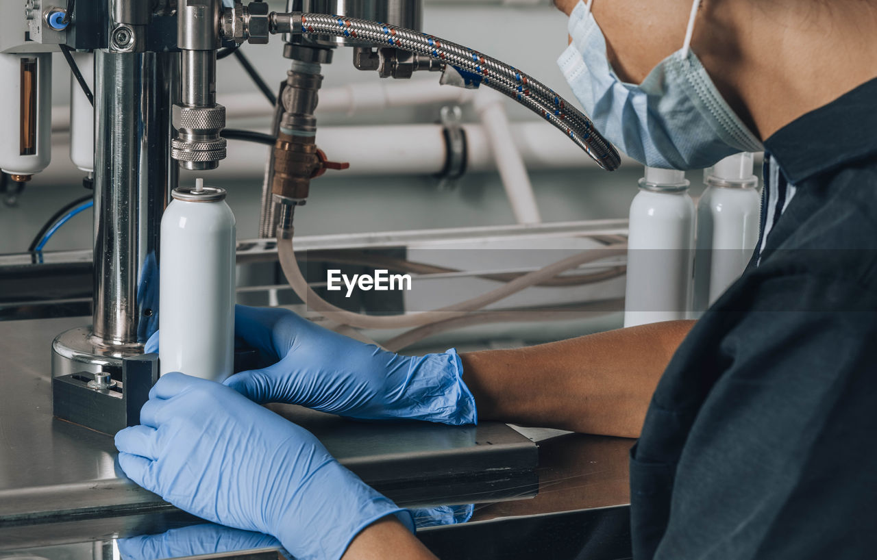 Unrecognizable woman in mask, cap, gloves works in production of cosmetics, pharmaceutical company