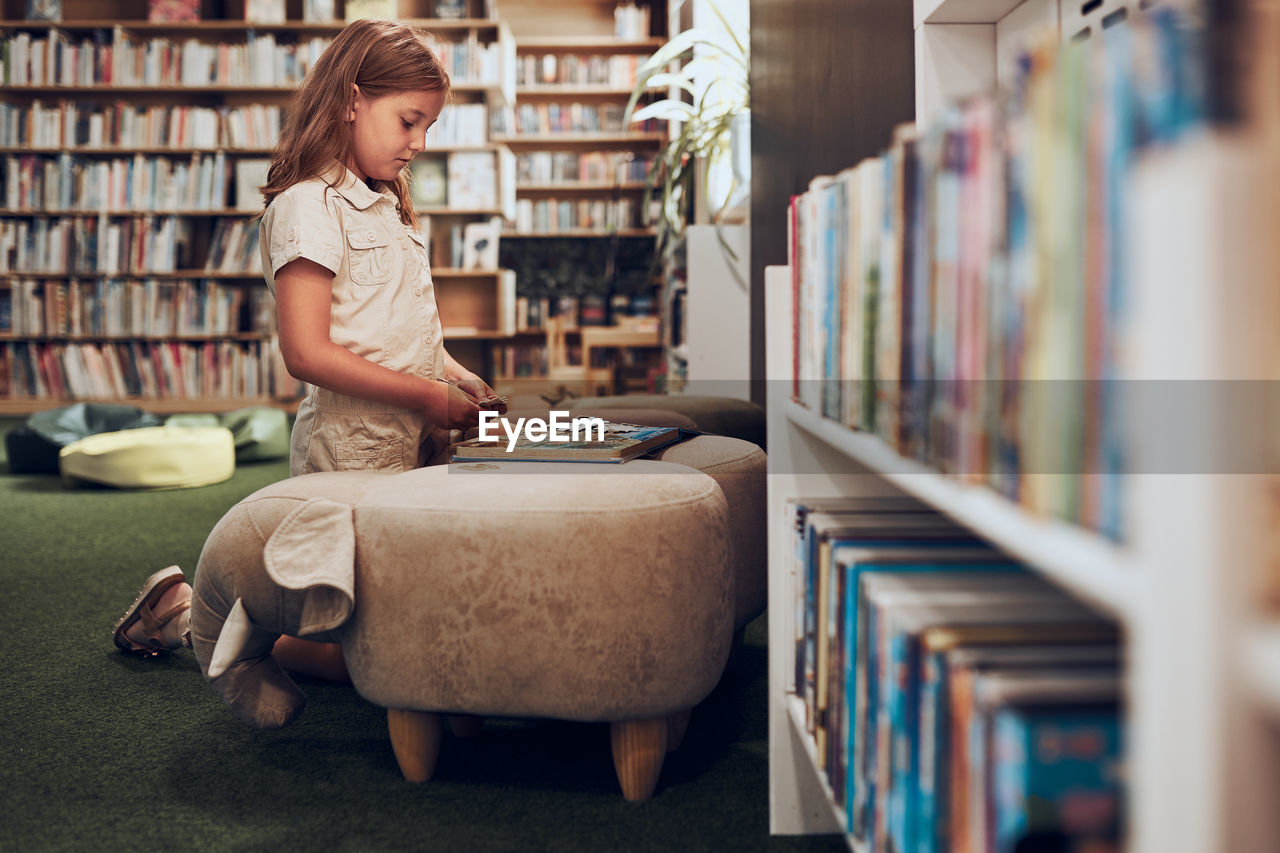 Schoolgirl doing puzzle and reading book in school library. primary school girl is involved in book