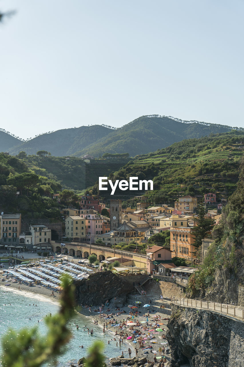 From above picturesque drone view of houses and beach of resort town located near sea against green mountains and sundown sky