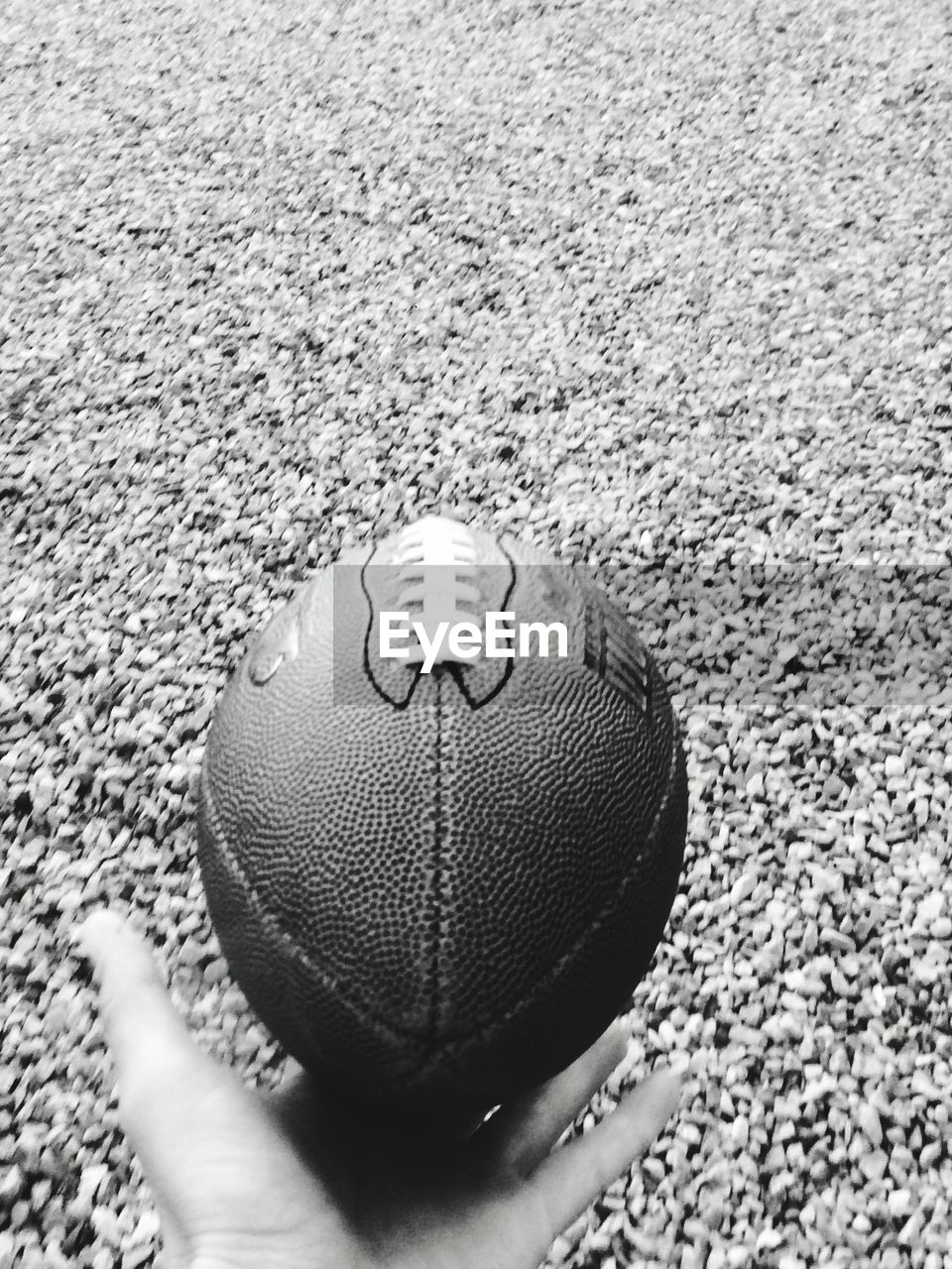 Cropped image of hand holding rugby ball over gravels