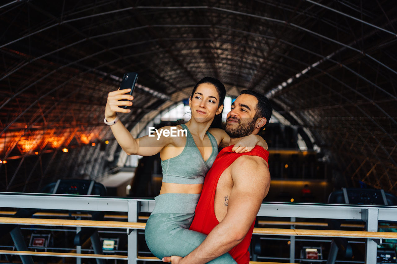Portrait of young couple in love standing in gym happy wearing gym clothes