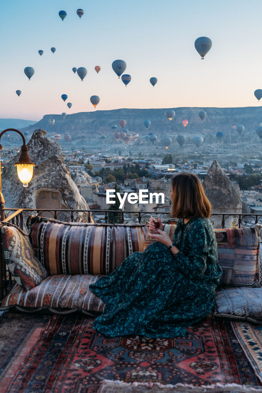 Woman drinking early morning tea with hot air balloons in cappadocia