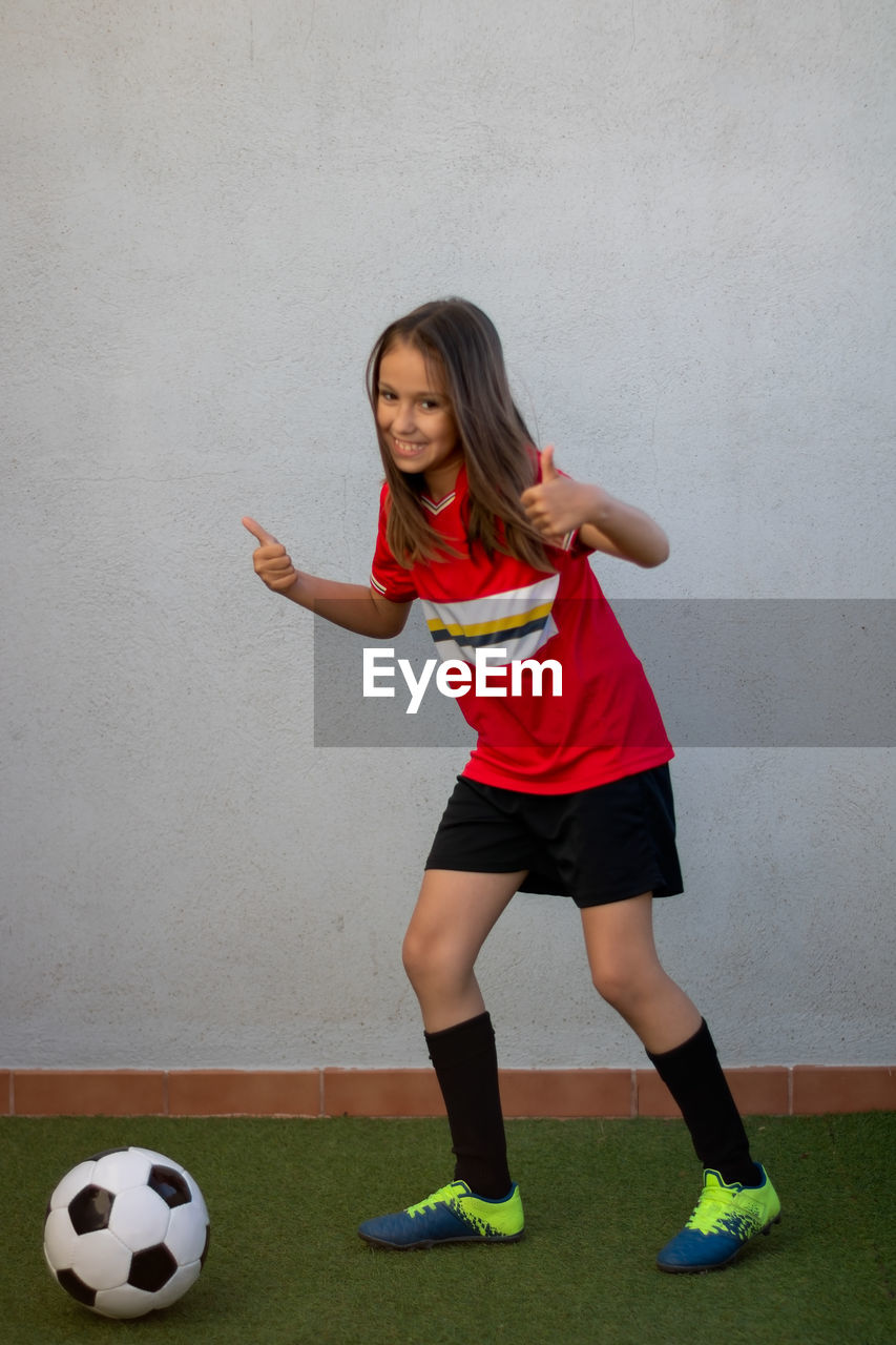 Portrait of smiling girl playing soccer against wall