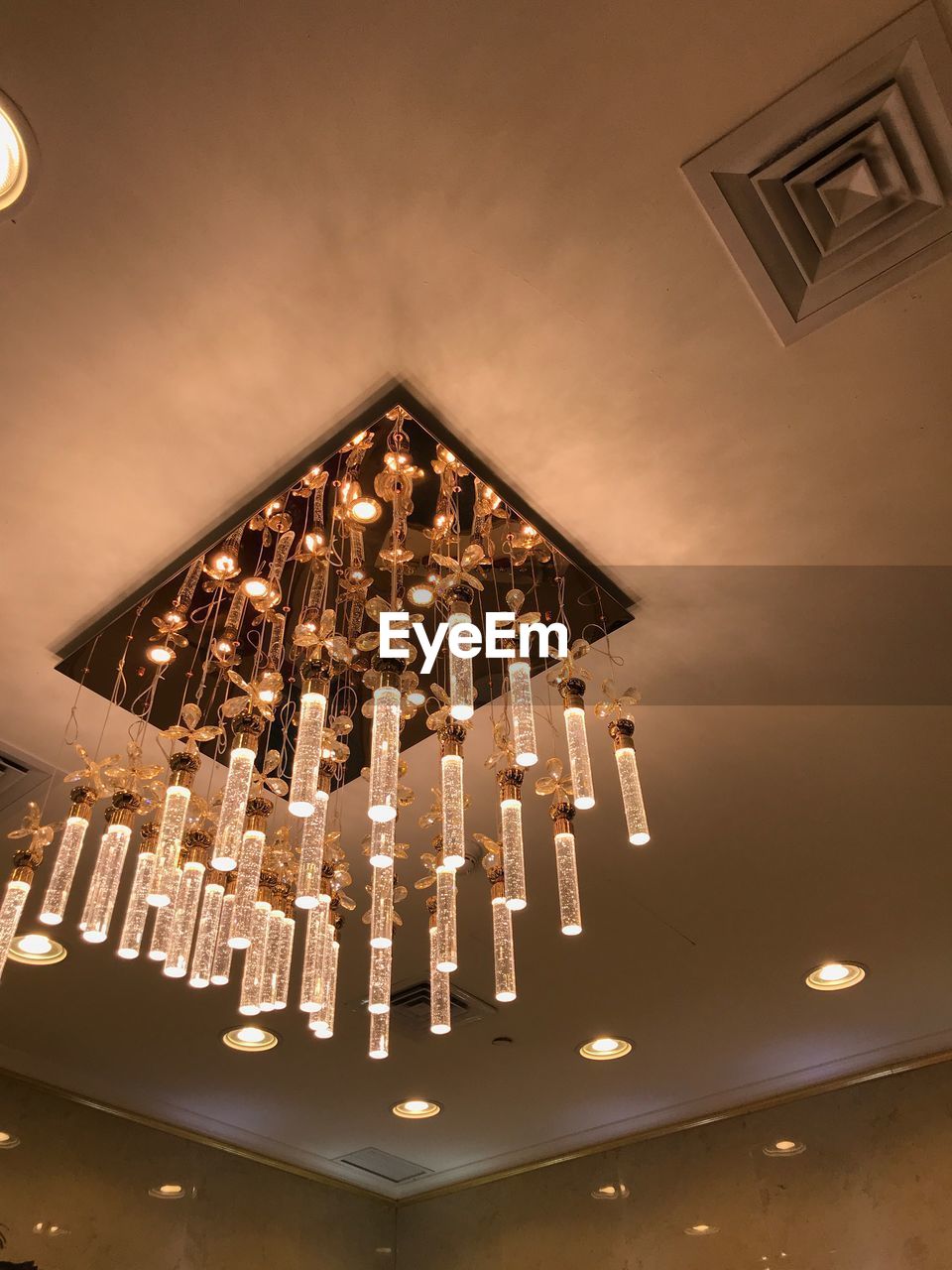 LOW ANGLE VIEW OF ILLUMINATED CHANDELIER HANGING ON CEILING AT HOME