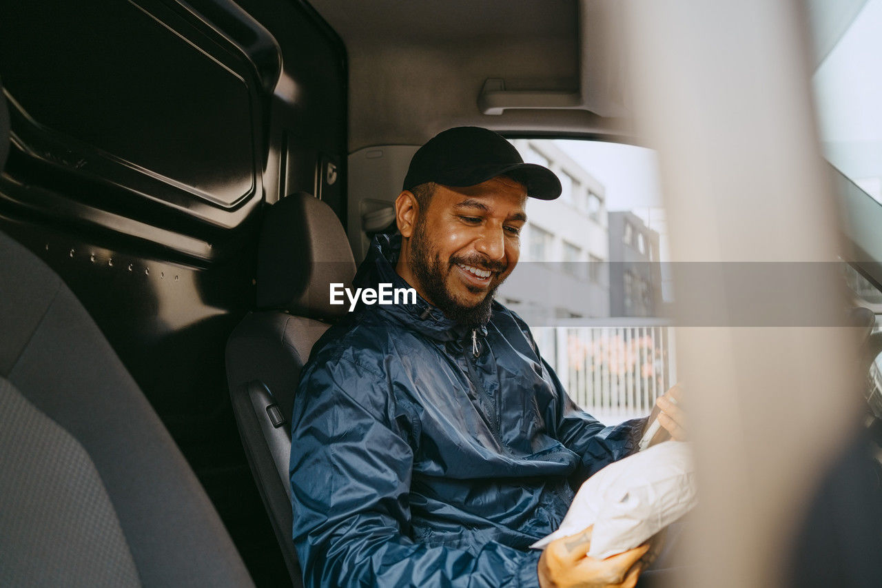 Smiling male delivery person holding parcel while sitting in van