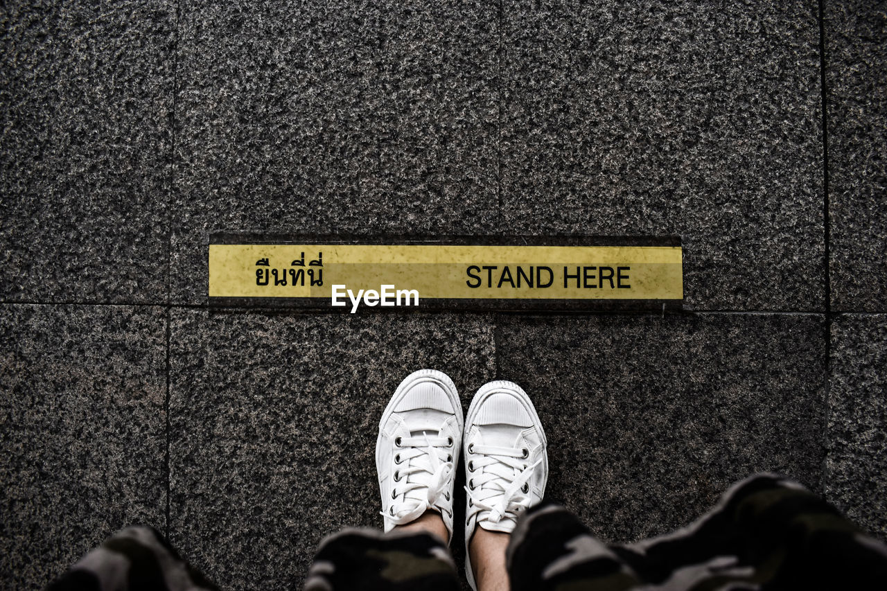 LOW SECTION OF MAN STANDING BY TEXT ON FLOORING