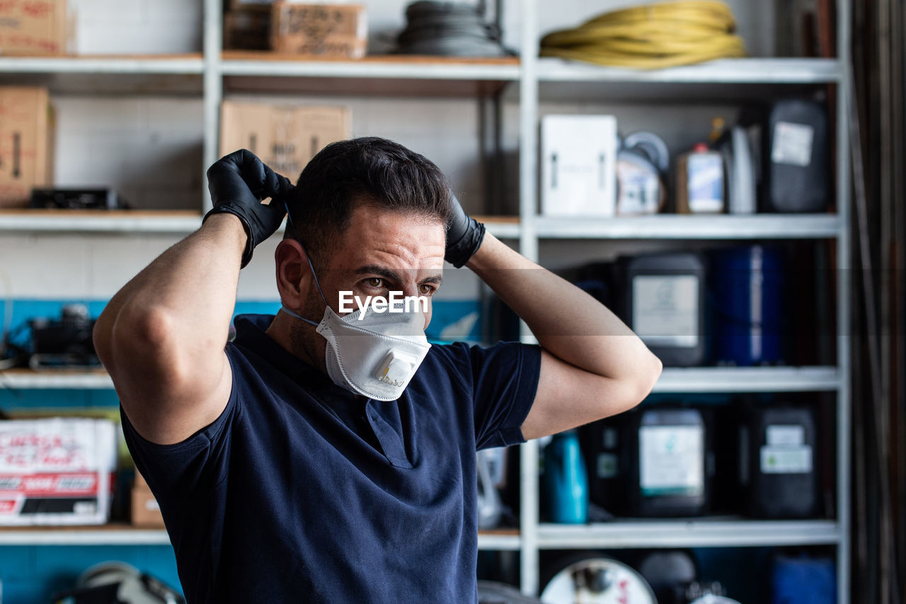 Male employee putting white face mask for work in garage