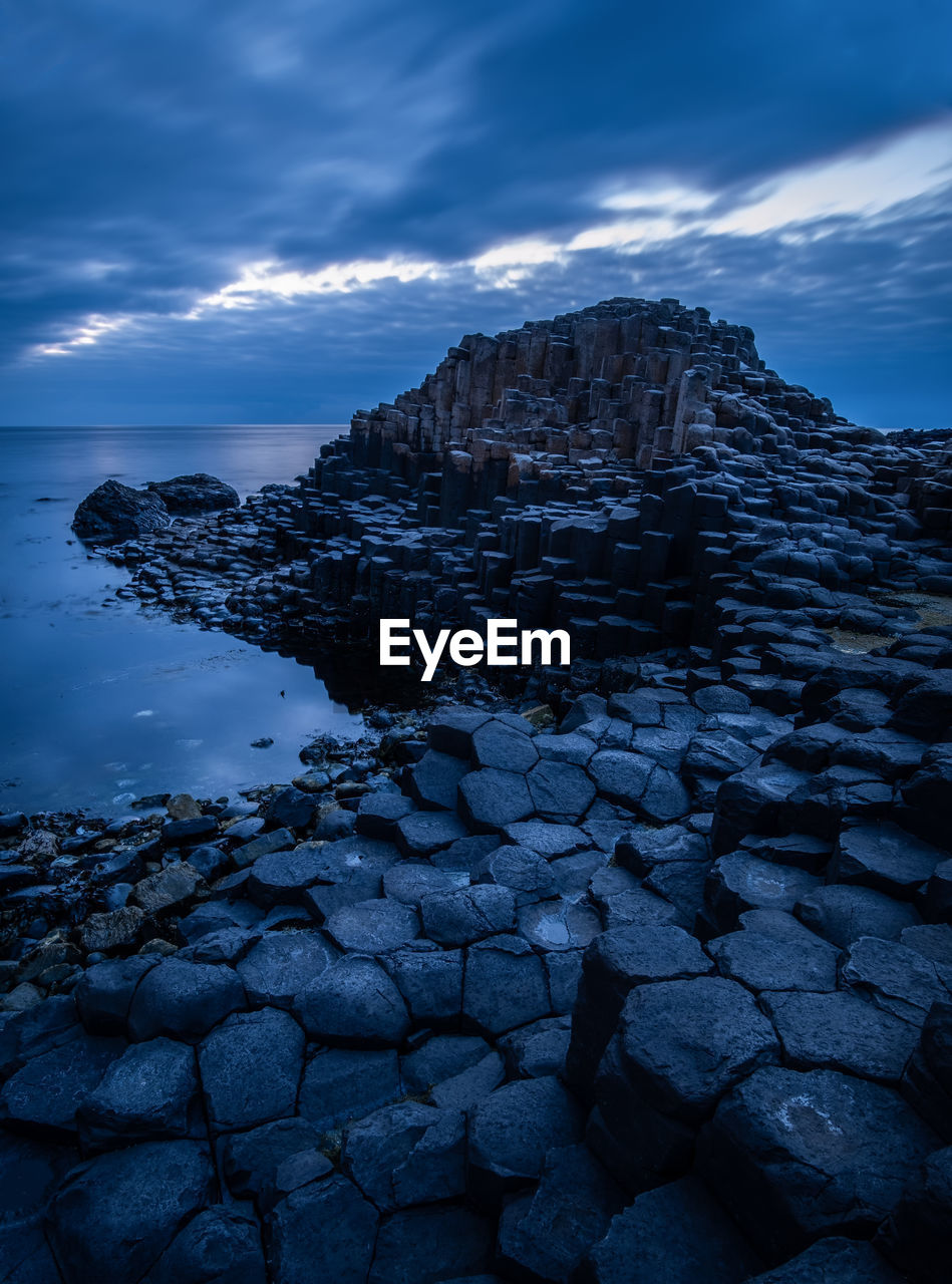 Scenic view of rock formations at beach against cloudy sky at dusk