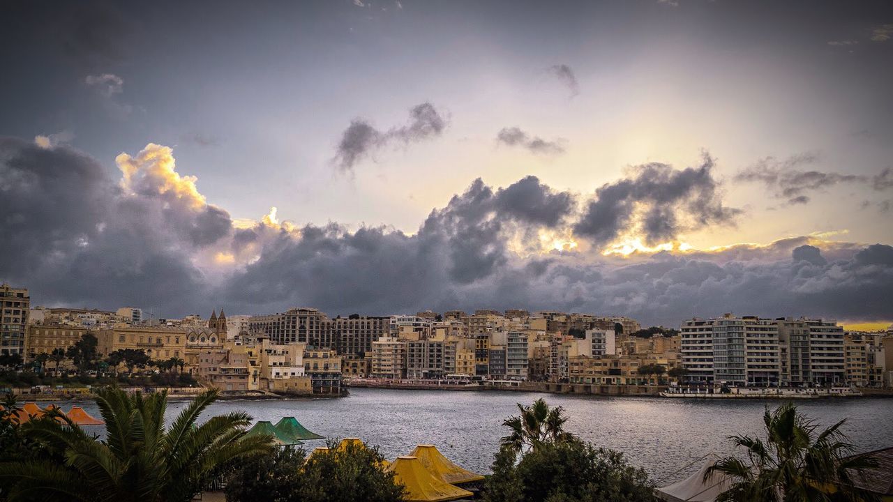 Buildings and river against cloudy sky
