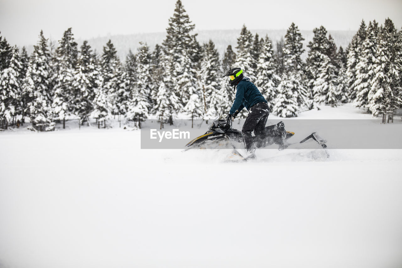 Side view of man snowmobiling on a snowy day.