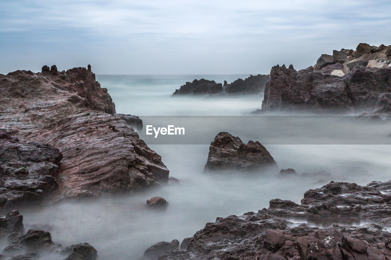 Scenic view of rock formations in sea against cloudy sky
