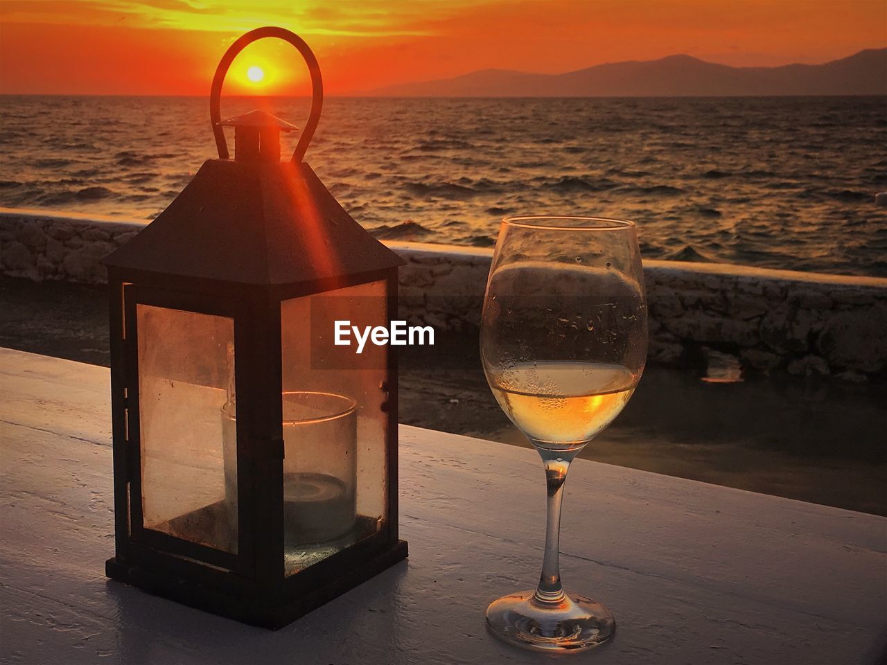 WINEGLASS ON TABLE AGAINST SEA DURING SUNSET