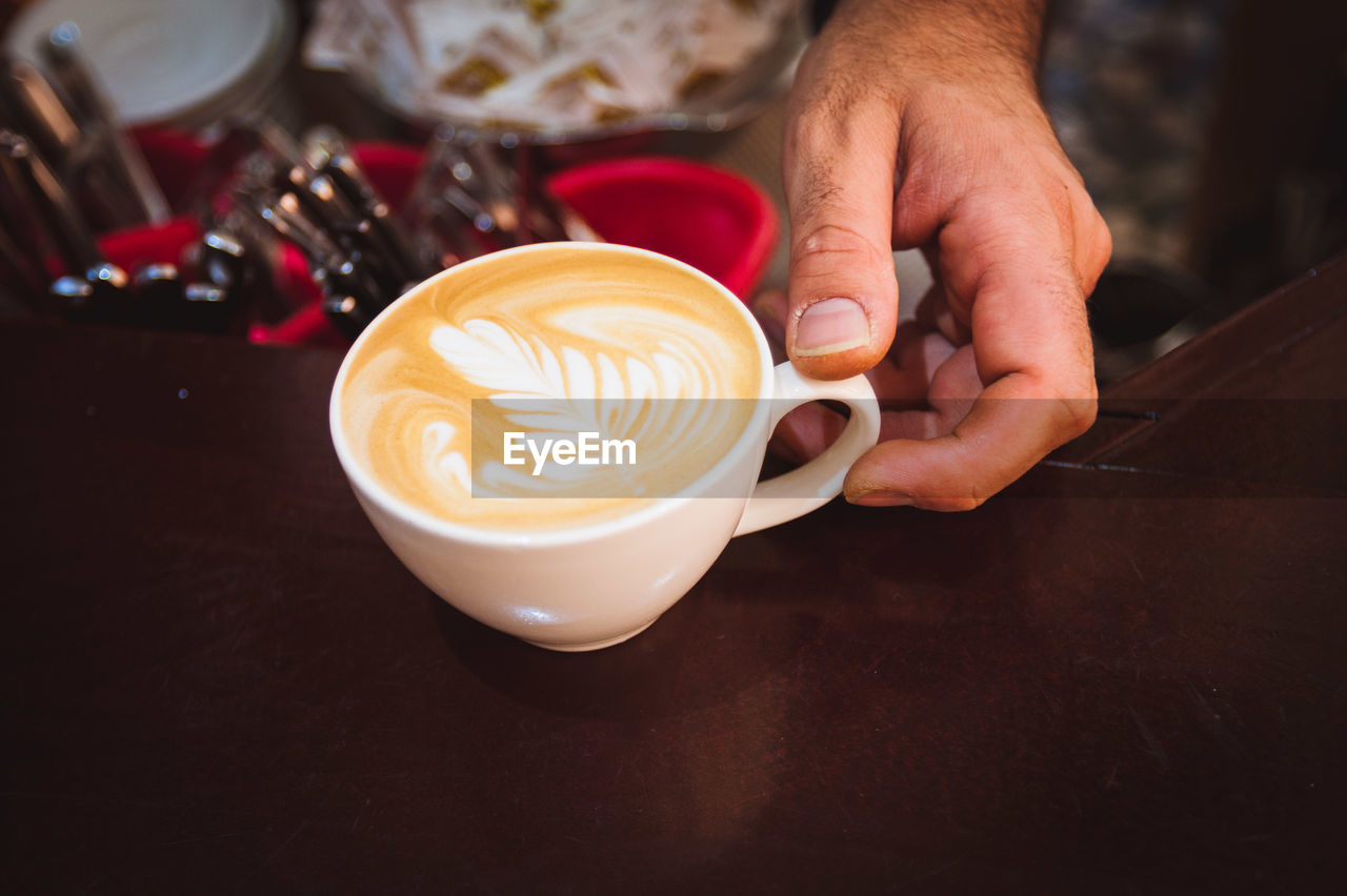 Cropped hand of barista holding coffee cup on table at cafe