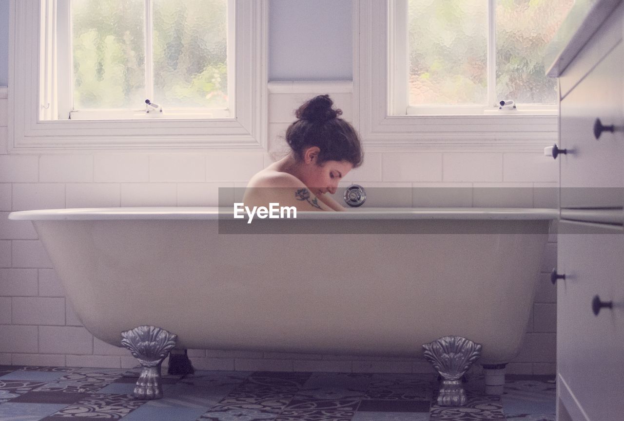 Side view of young woman sitting in bathtub at home