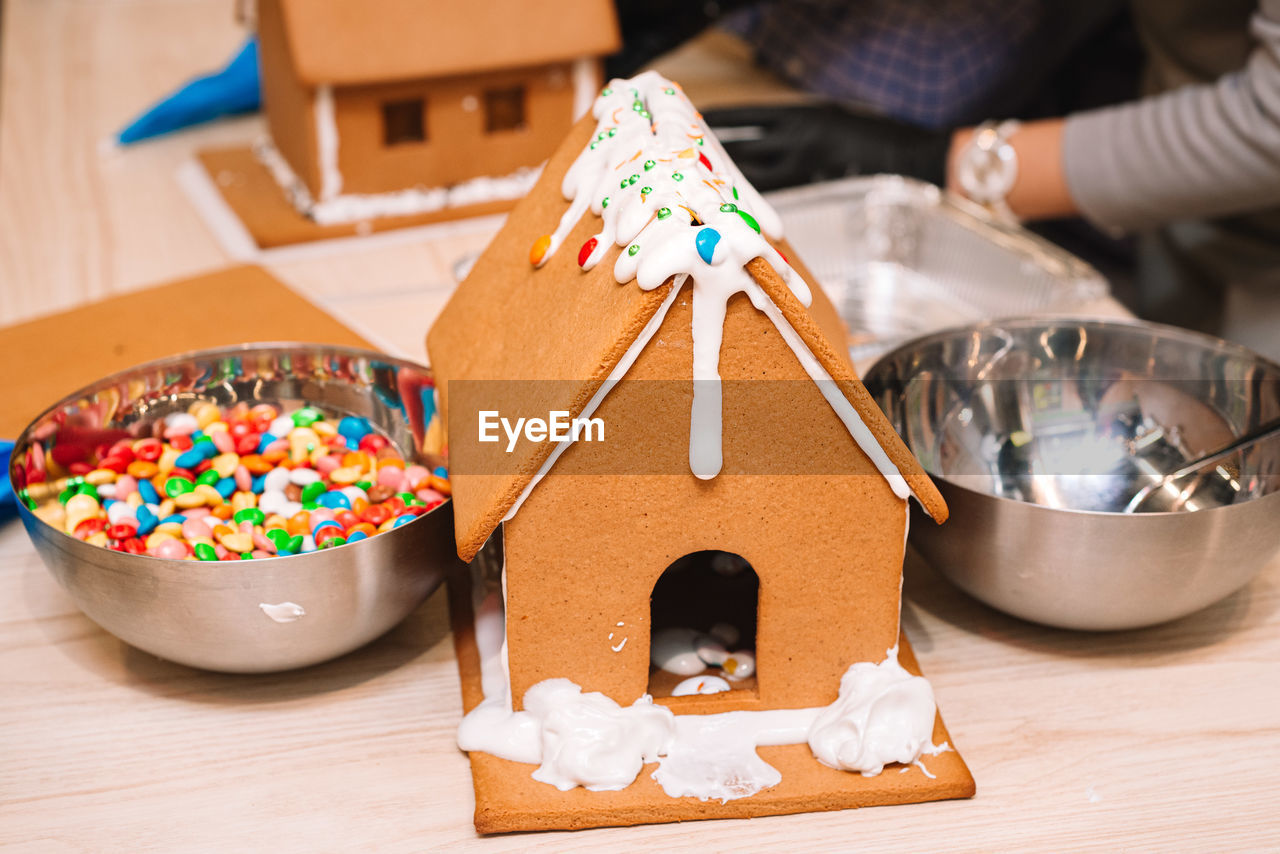 gingerbread house, sweet food, food, gingerbread, food and drink, sweet, indoors, dessert, celebration, table, multi colored, baked, cake, wood, holiday, childhood, child, tradition, creativity, one person, icing, decoration, candy, chocolate, close-up, focus on foreground