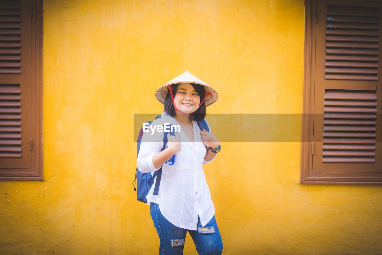 Portrait of smiling woman standing against yellow wall