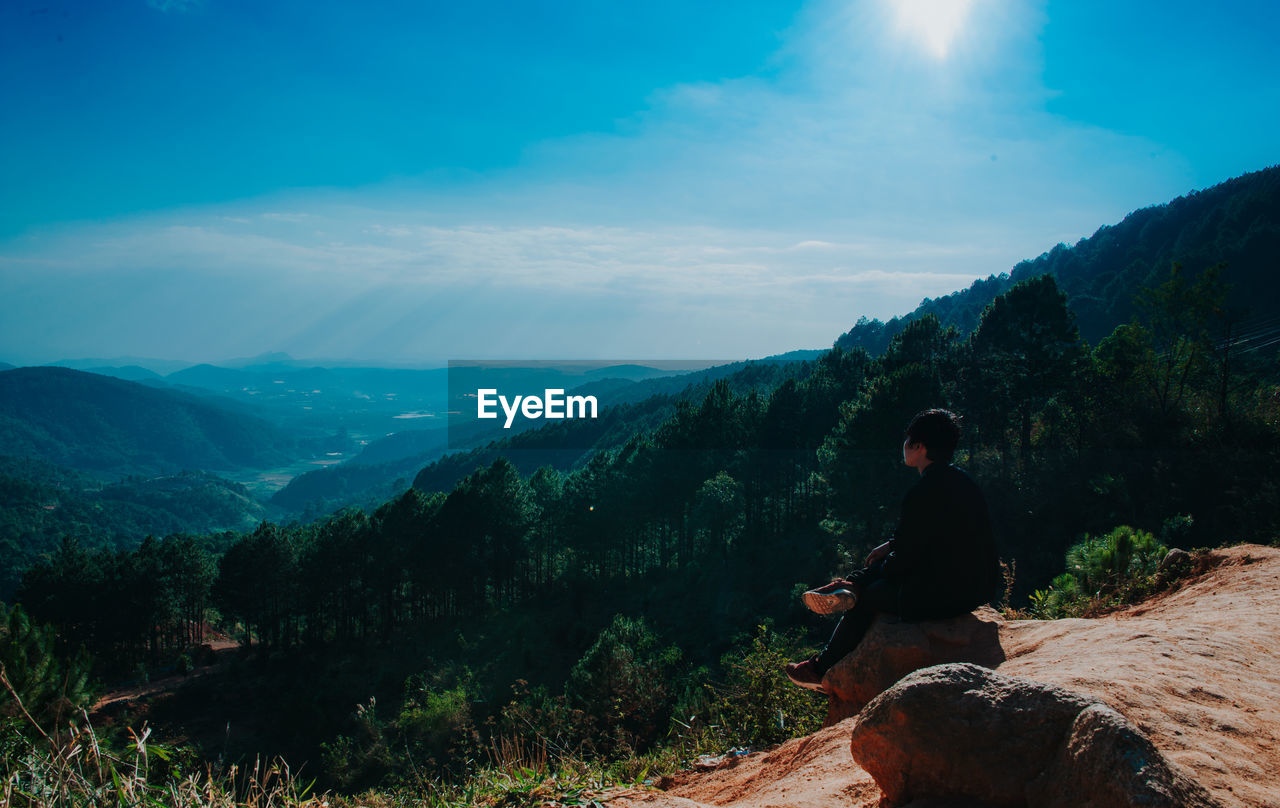 Man sitting on mountain against sky