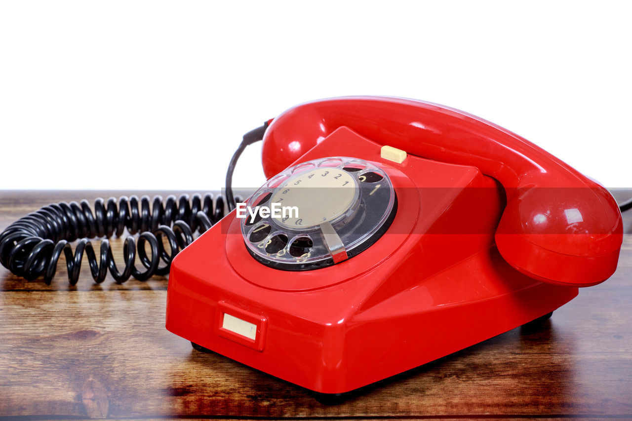 Close-up of red rotary phone on wooden table against white background