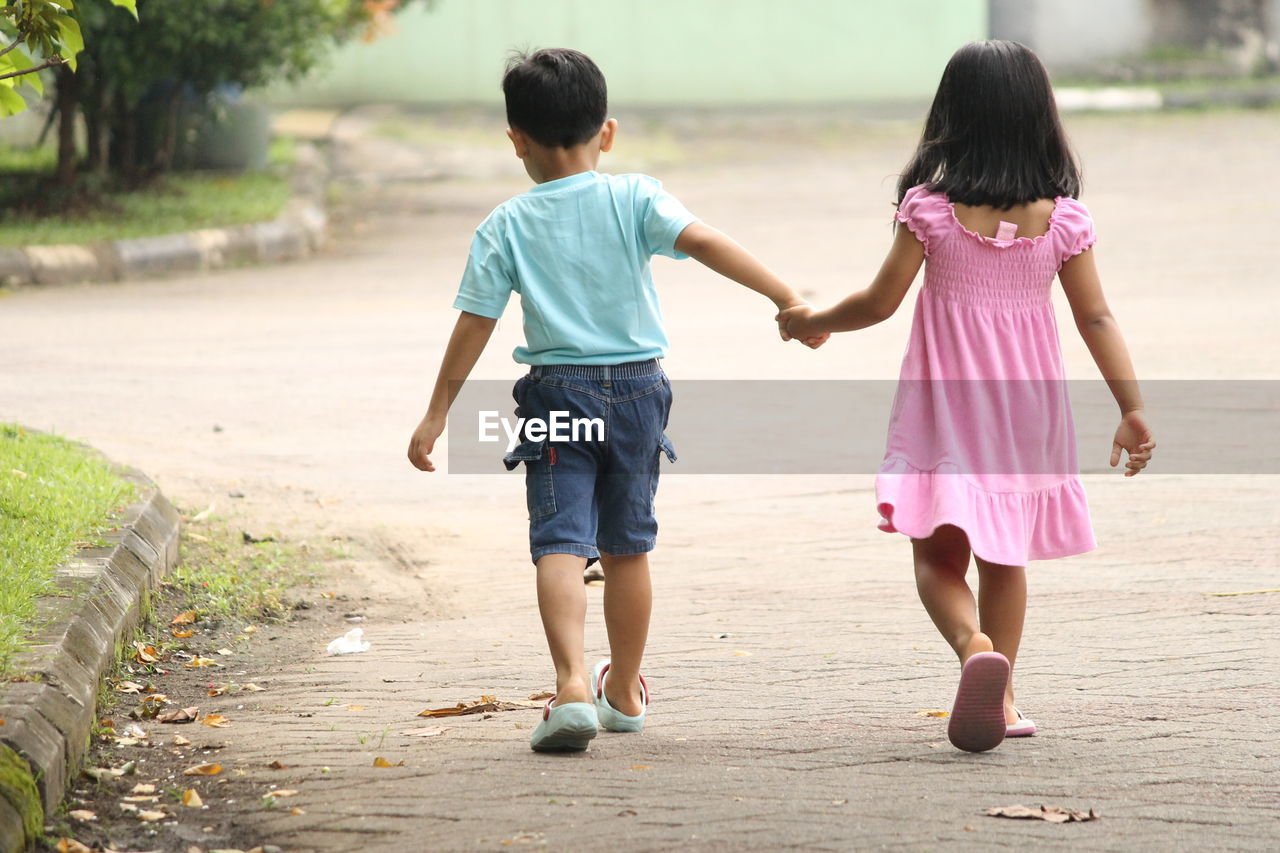 Rear view of brother and sister walking on road