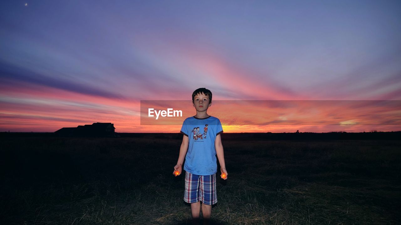 Boy holding lit candles while standing on grassy field at dusk