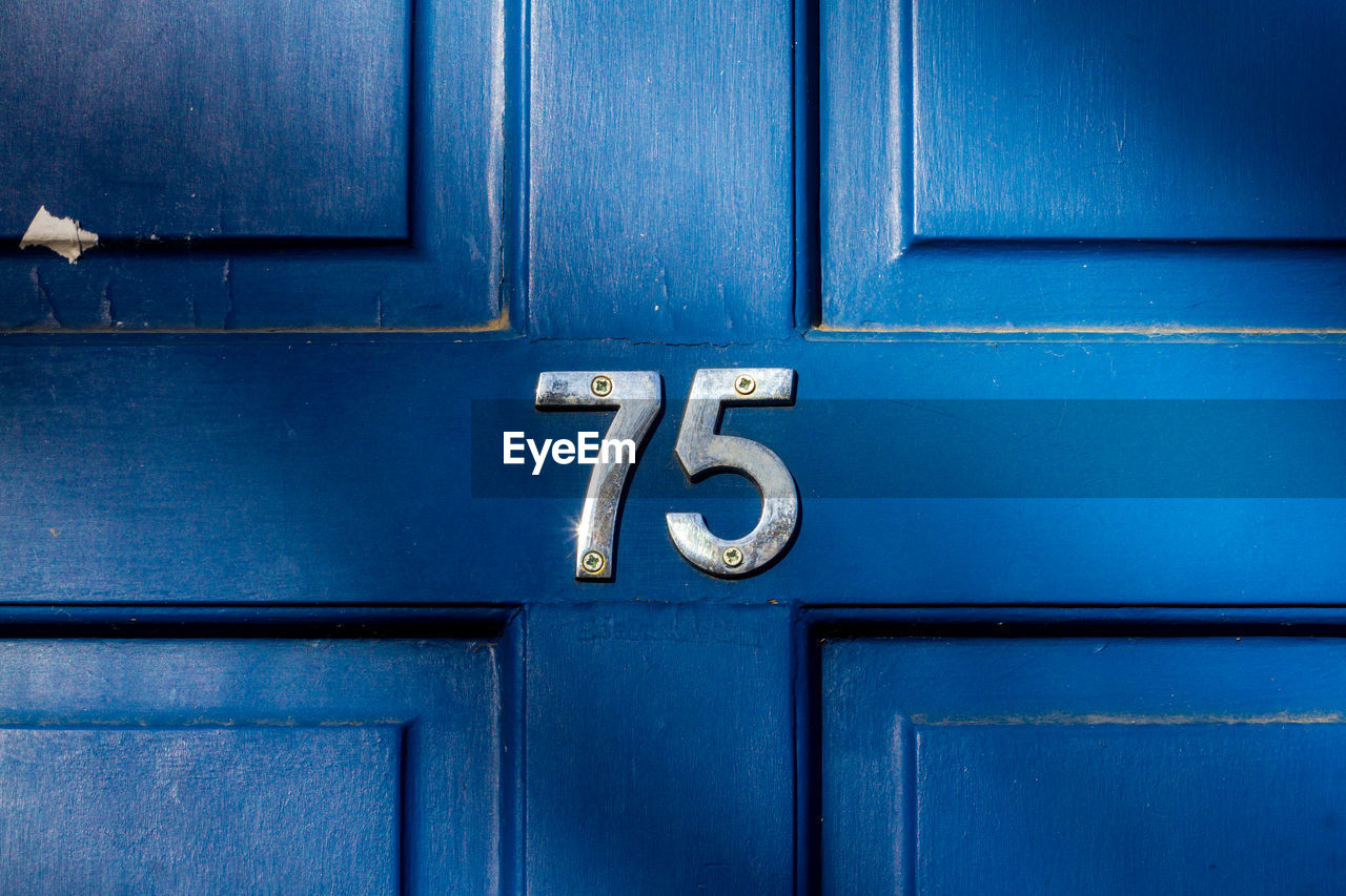 House number 75 on a blue wooden front door in london 