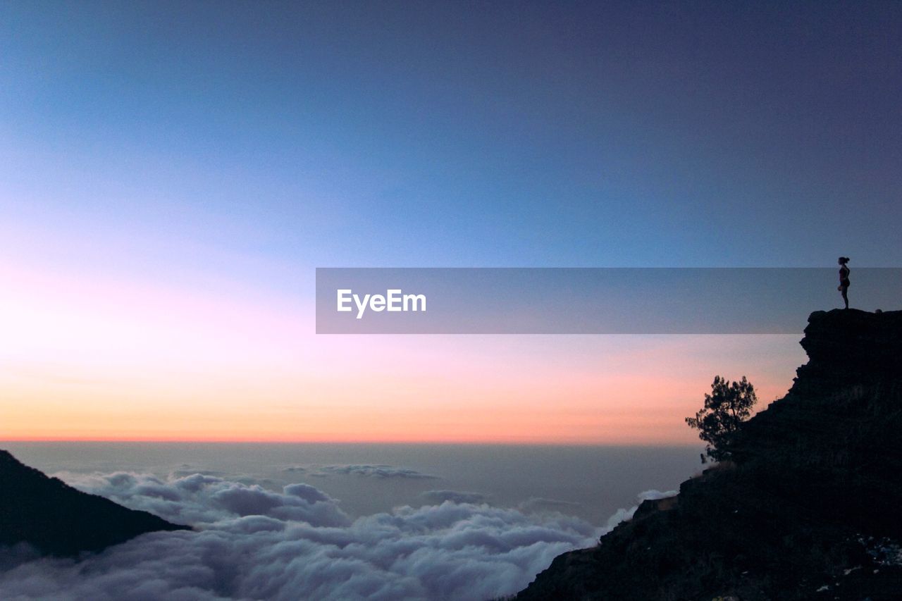 Silhouette woman standing on cliff against blue sky during sunset