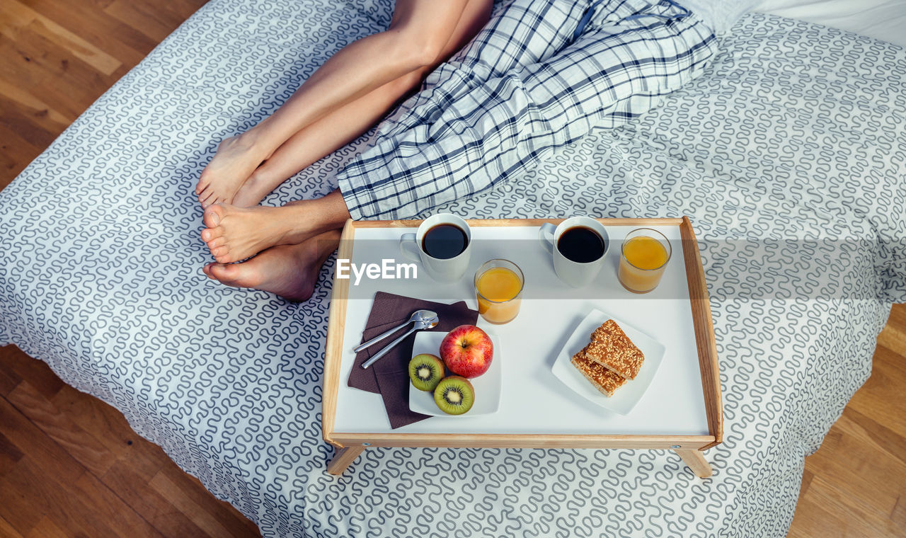 Low section of couple with breakfast on bed at home