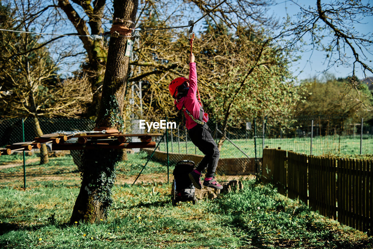 Little girl with protections practicing climbing between trees with ropes and nets