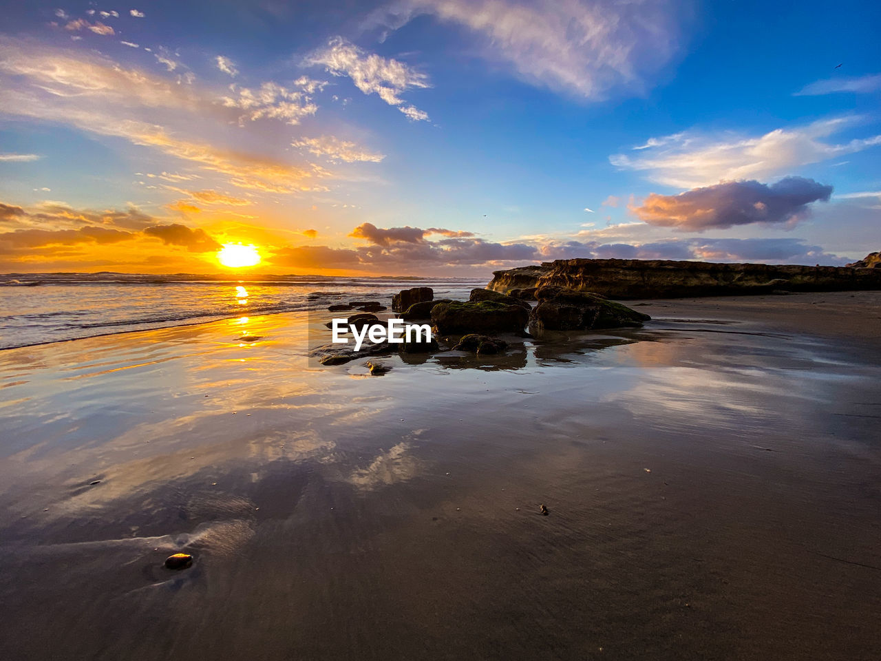 Reflecting sunset off sand and rocks with clouds at swamis beach in encinitas, san diego, california