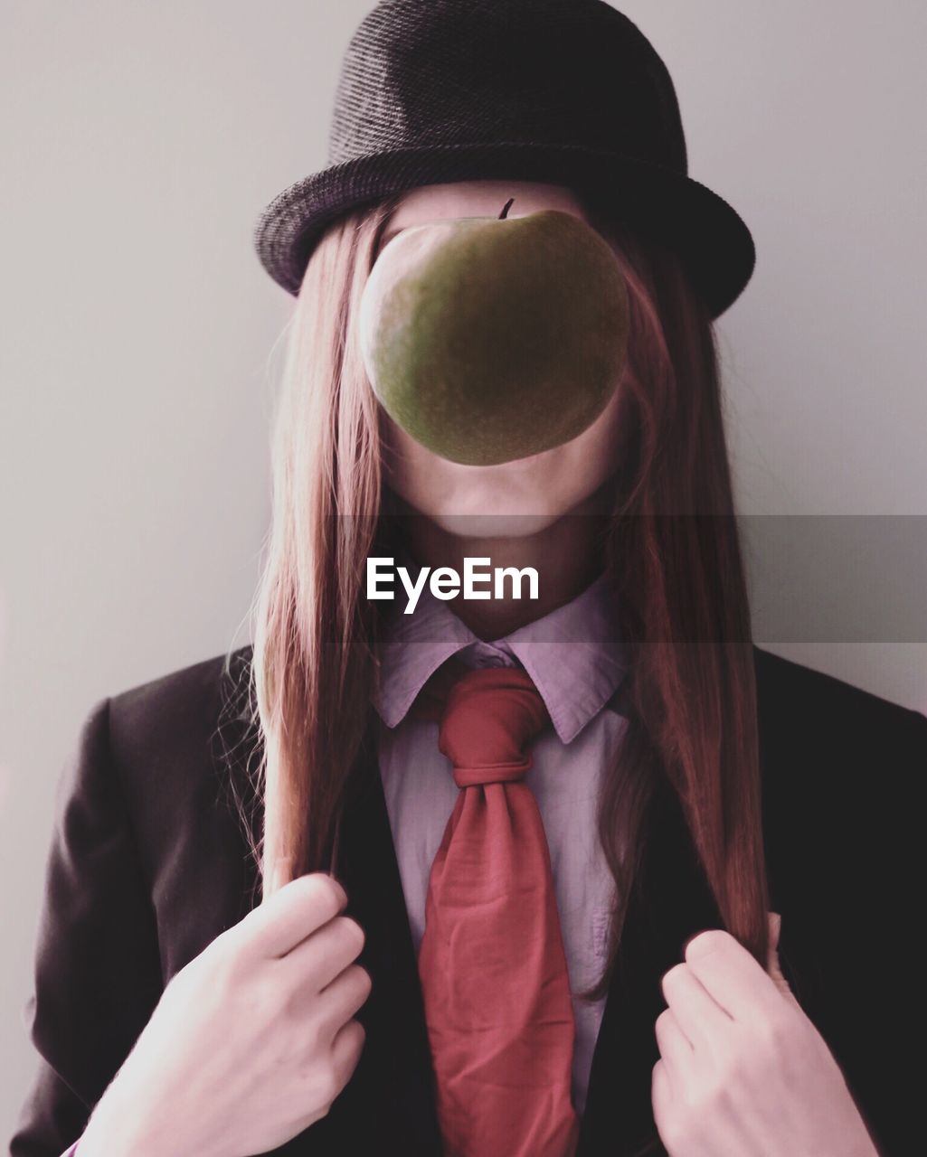 Woman with apple in front of face against gray background