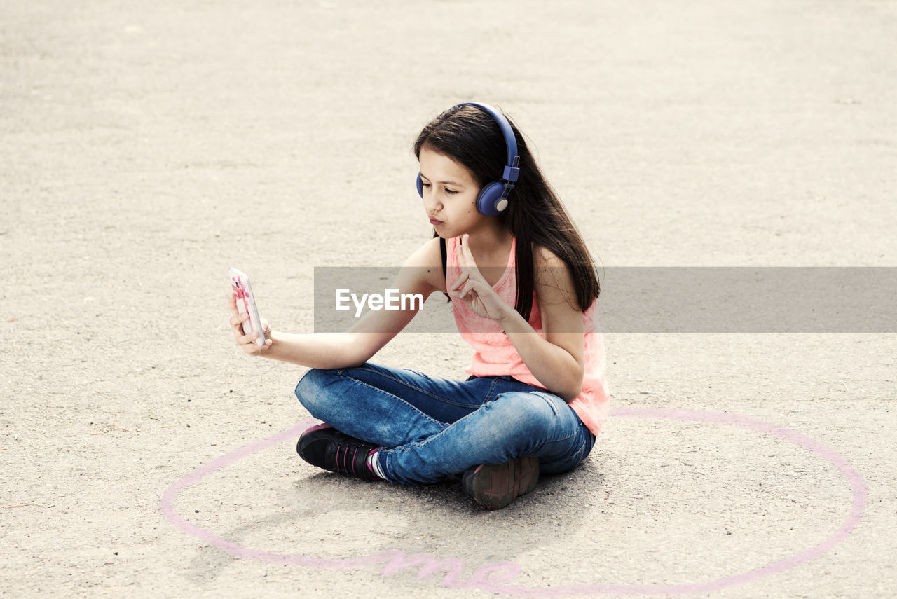 Girl gesturing peace sign while taking selfie on footpath