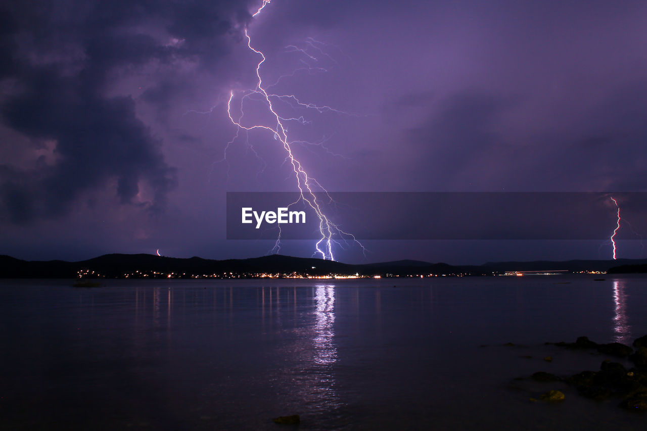 Lightning over illuminated cityscape against dramatic sky