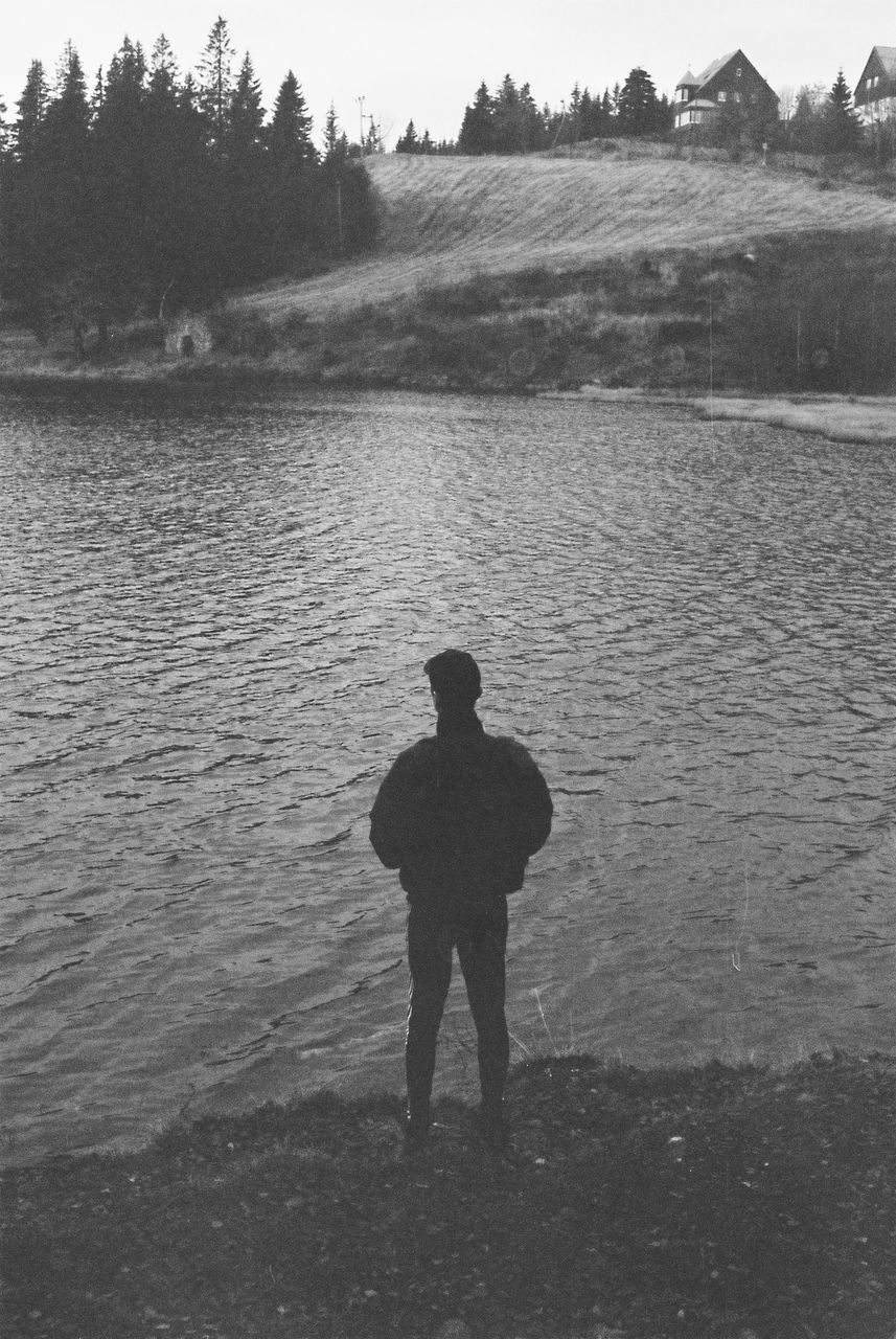 Full length rear view of man standing on riverbank against sky
