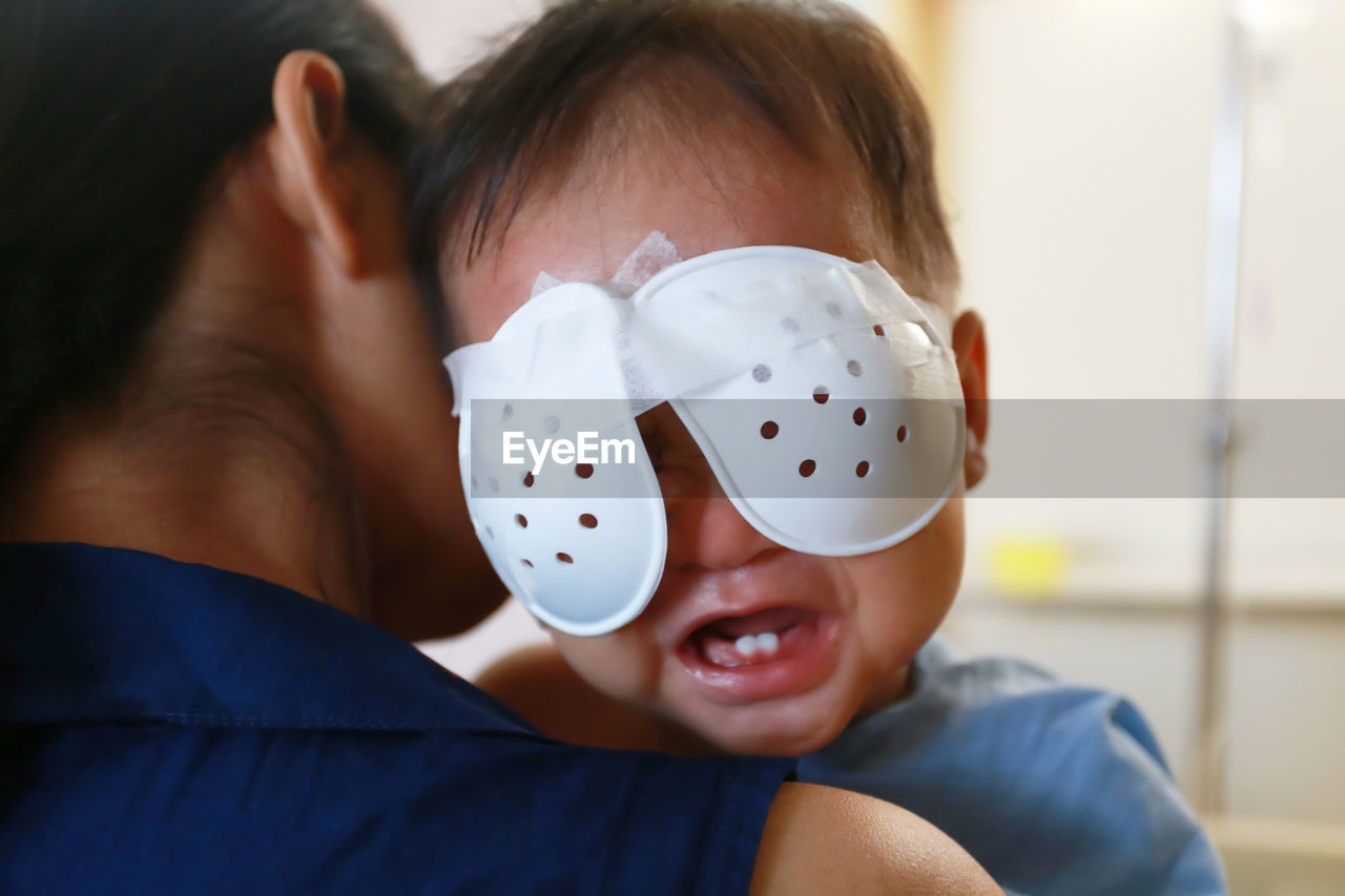Close-up of mother carrying baby boy with bandage on eyes