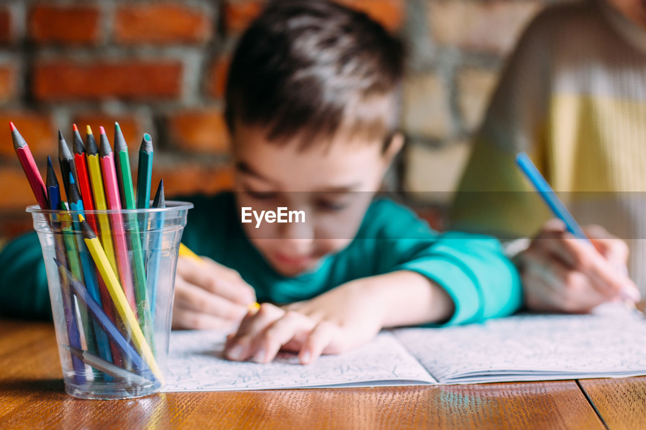 Portrait of a cute happy preschool boy at home or in a cafe draws.